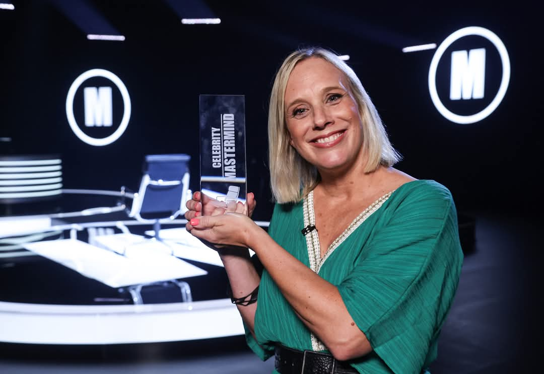 Kirsten blonde short hair and a green dress holds up her Mastermind trophy